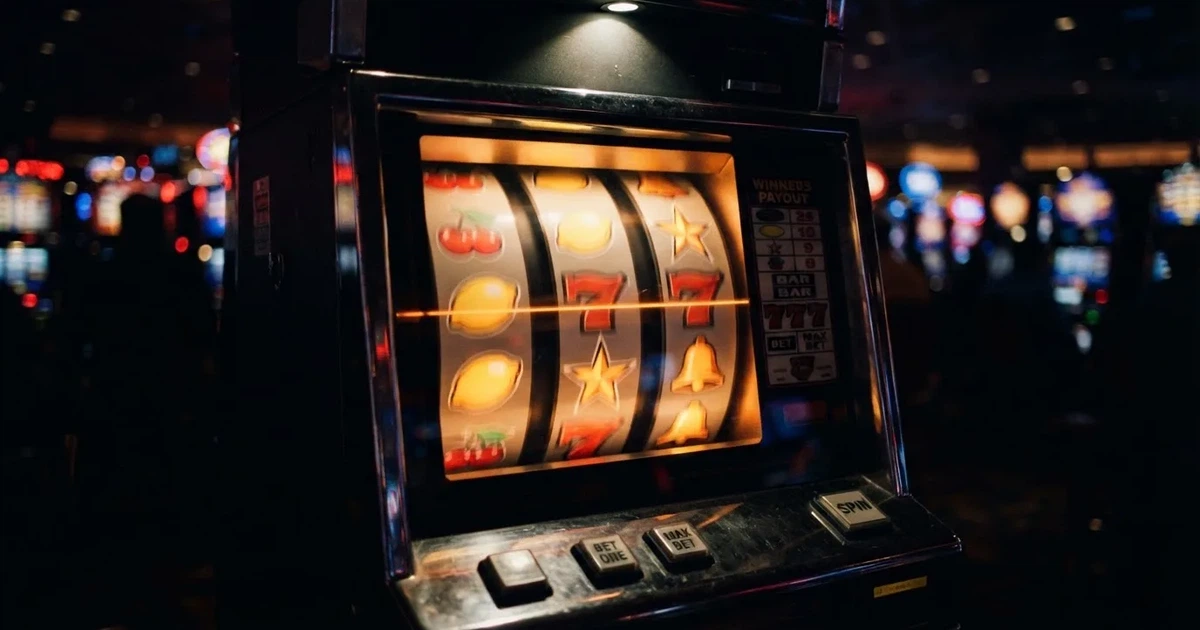 Nahaufnahme bunt beleuchteter Spielautomaten-Walzen mit Frucht- und Stern-Symbolen in einem dunklen Casino-Saal.